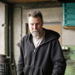 Serious adult bearded mechanic in black workwear standing in spacious workshop and looking at camera