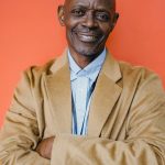Happy confident bald African American male boss in formal apparel looking at camera with crossed arms on orange background